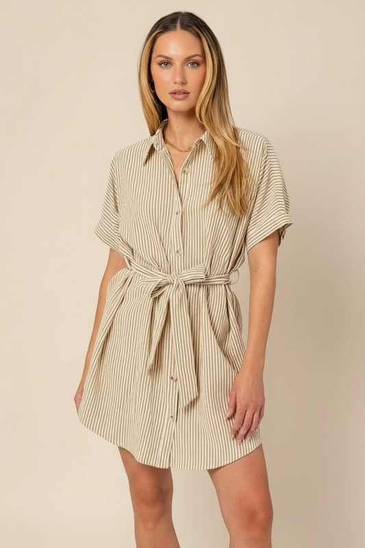 Woman wearing a beige and white striped shirt dress on a plain background