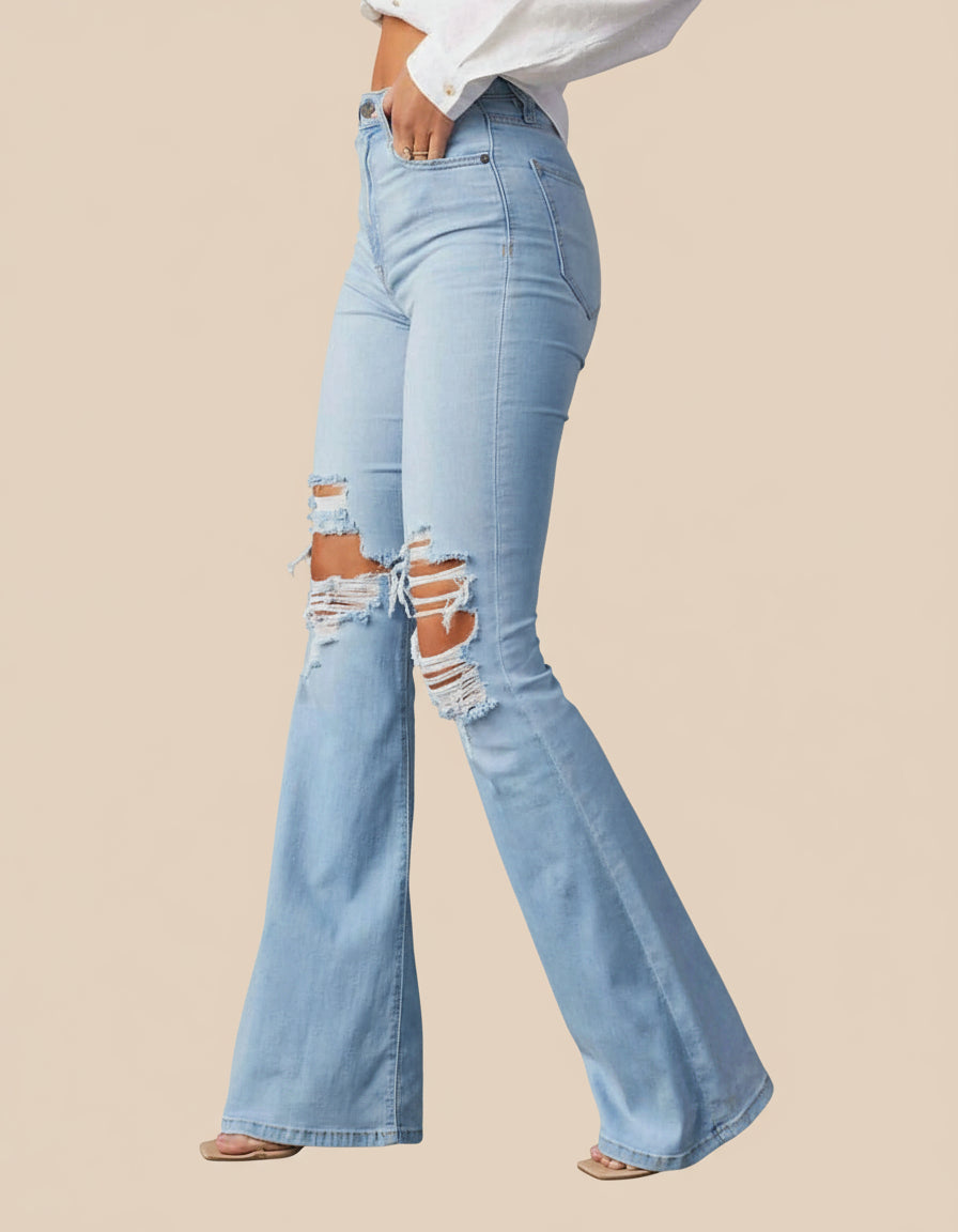Light blue flared jeans with distressing on a tan background