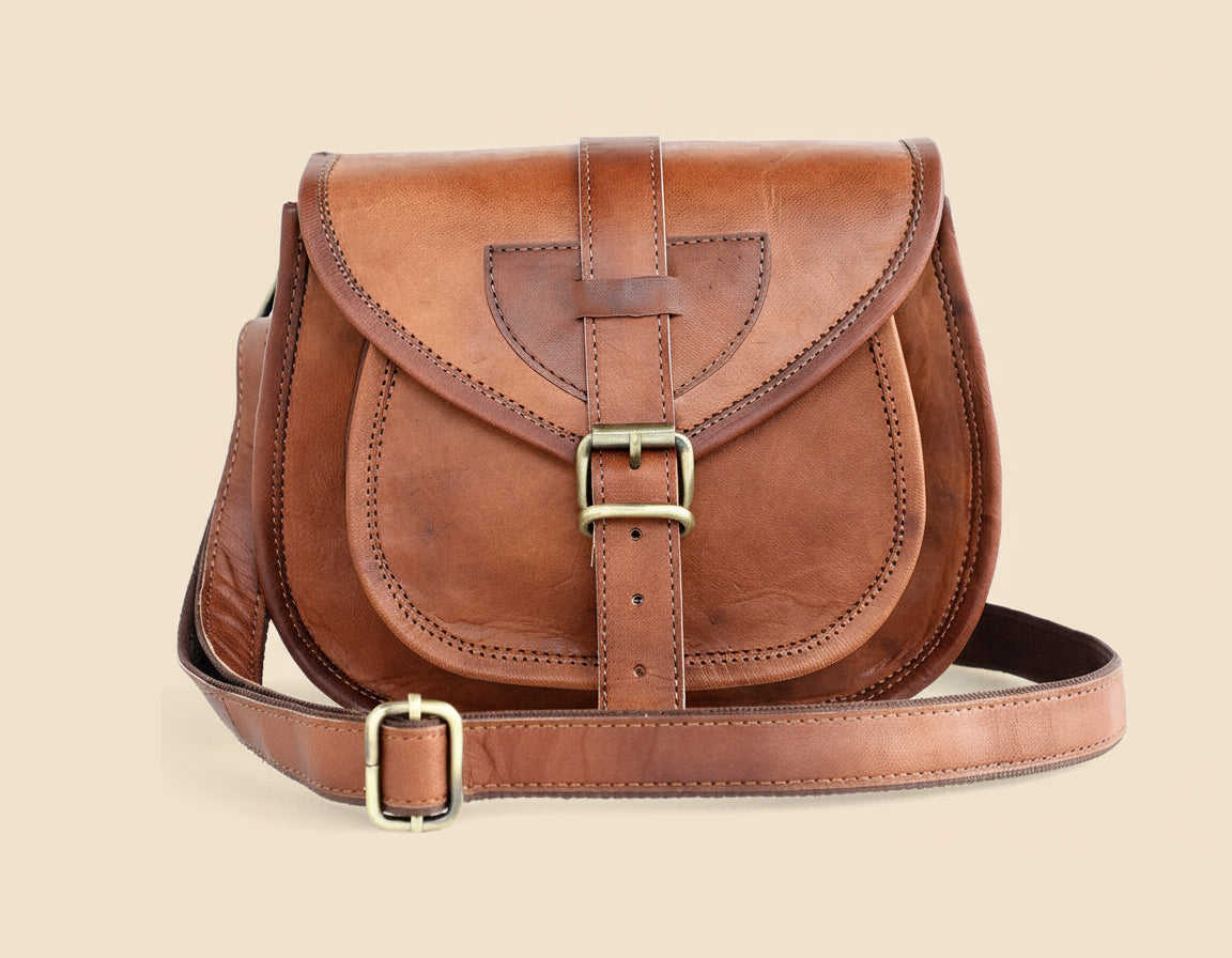 Brown leather satchel bag with gold buckles on a tan background