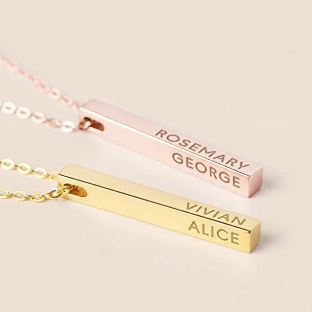 Two gold bar necklaces with engraved names on a light tan background