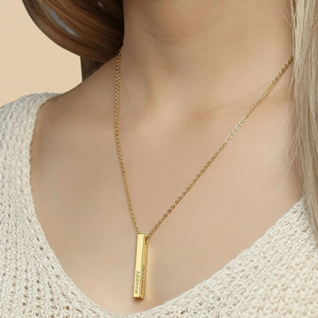 Gold necklace with a vertical bar pendant on a person wearing a white textured top.