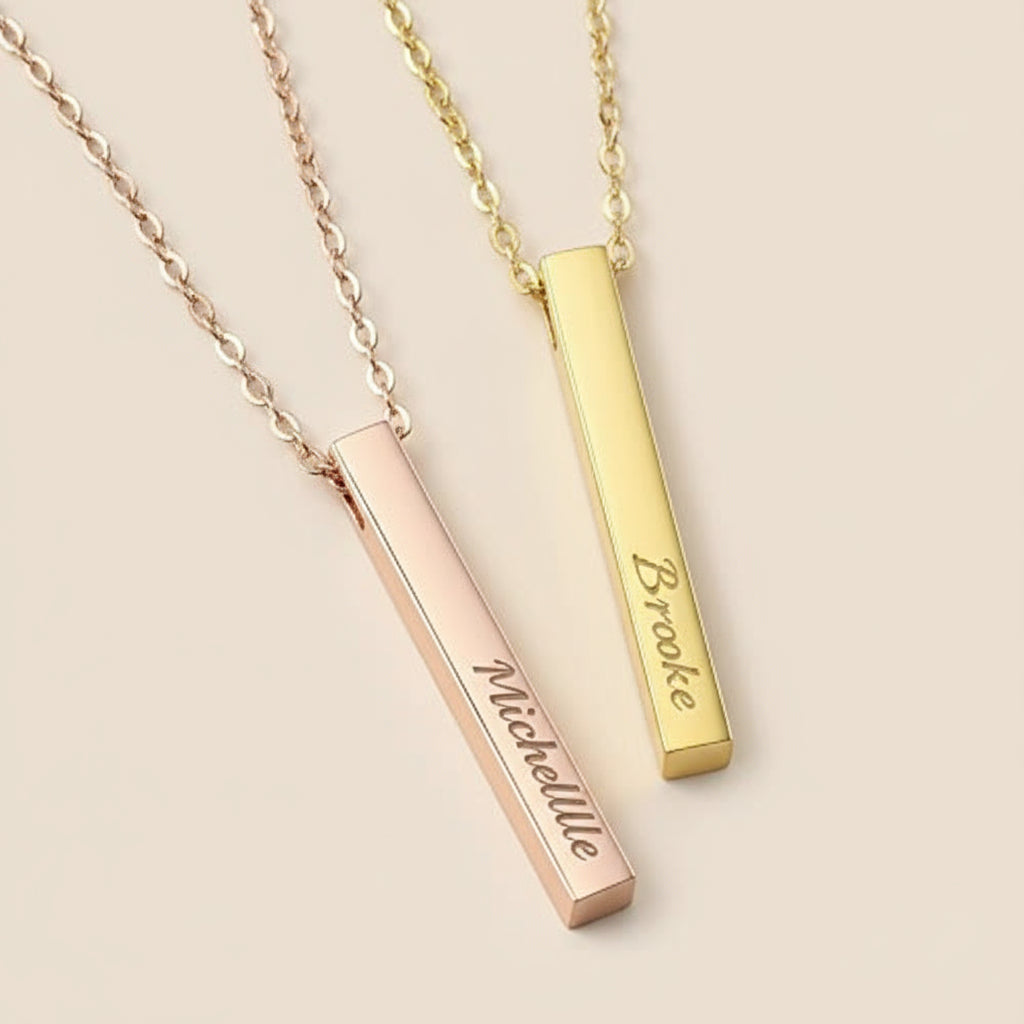 Two gold and rose gold necklaces with engraved names on a light tan background