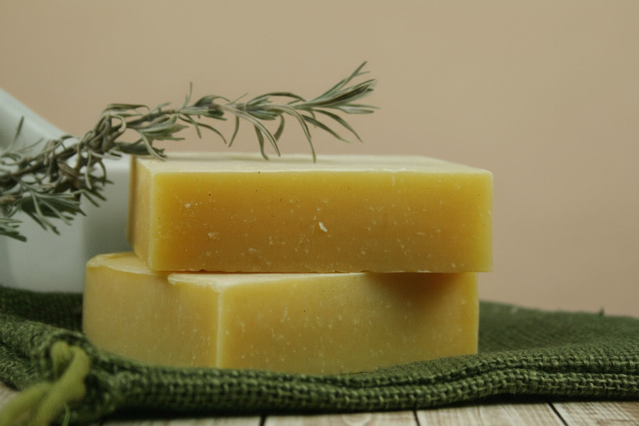two bars of yellow soap stacked on a green towel with a sprig of rosemary.