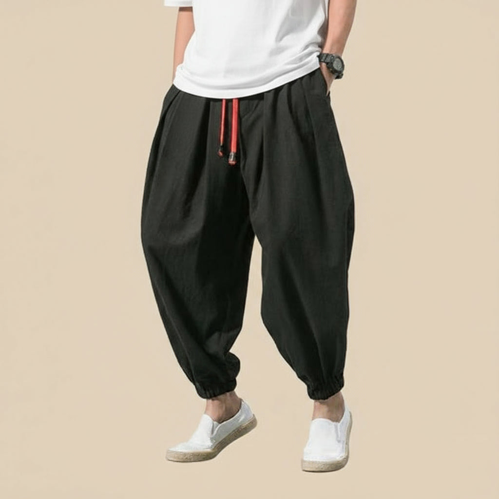 Person wearing black harem pants with a white shirt on a light tan background