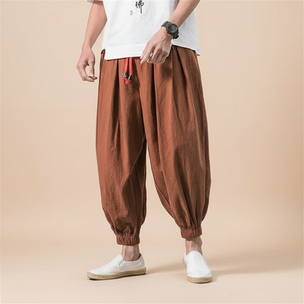 Person wearing brown baggy pants and white shoes on a light tan background