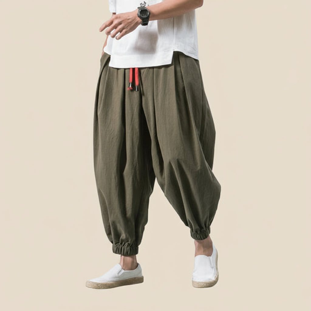 Person wearing olive green baggy pants with a white shirt on a light tan background