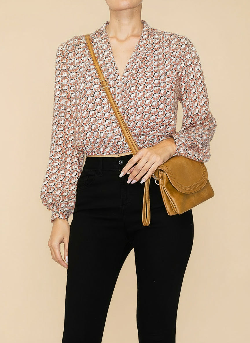 Person wearing a floral blouse and black pants with a brown leather bag on a white background