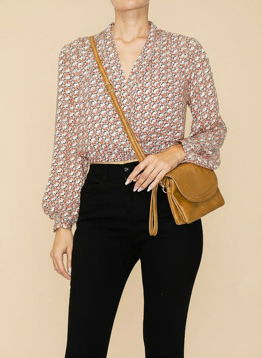 Person wearing a floral blouse and black pants with a brown leather bag on a white background