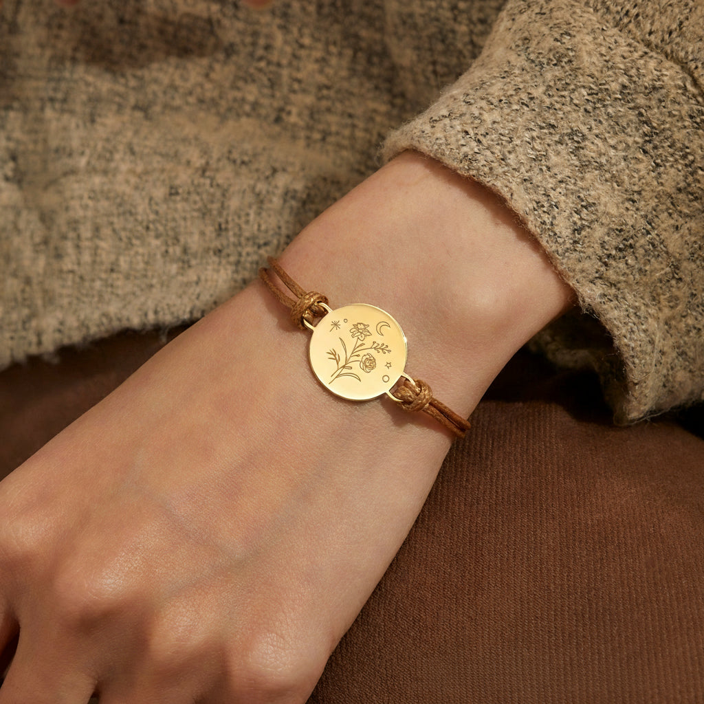 Gold bracelet with a circular emblem on a wrist, worn by a person in a textured garment.