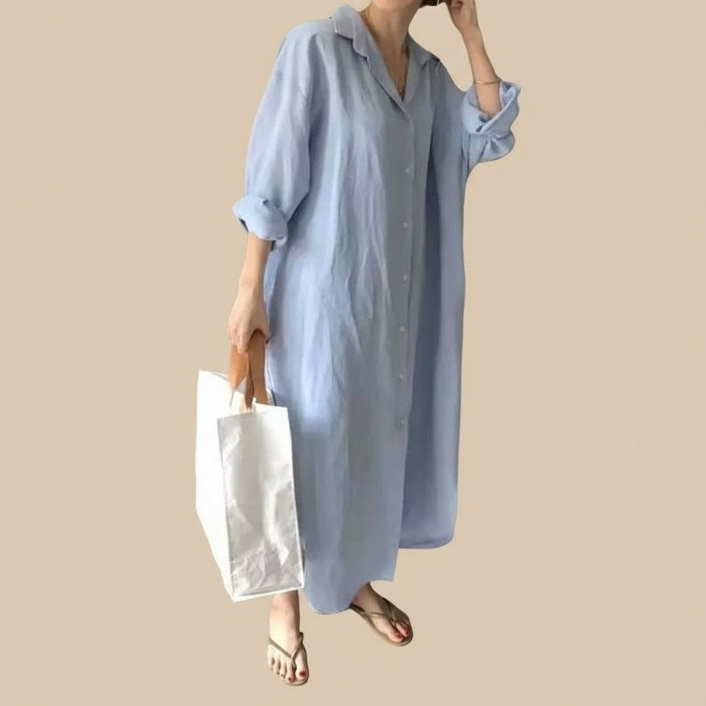 Person wearing a long light blue dress holding a white bag indoors.