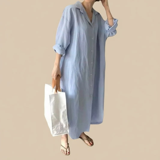 Person wearing a long light blue dress holding a white bag indoors.