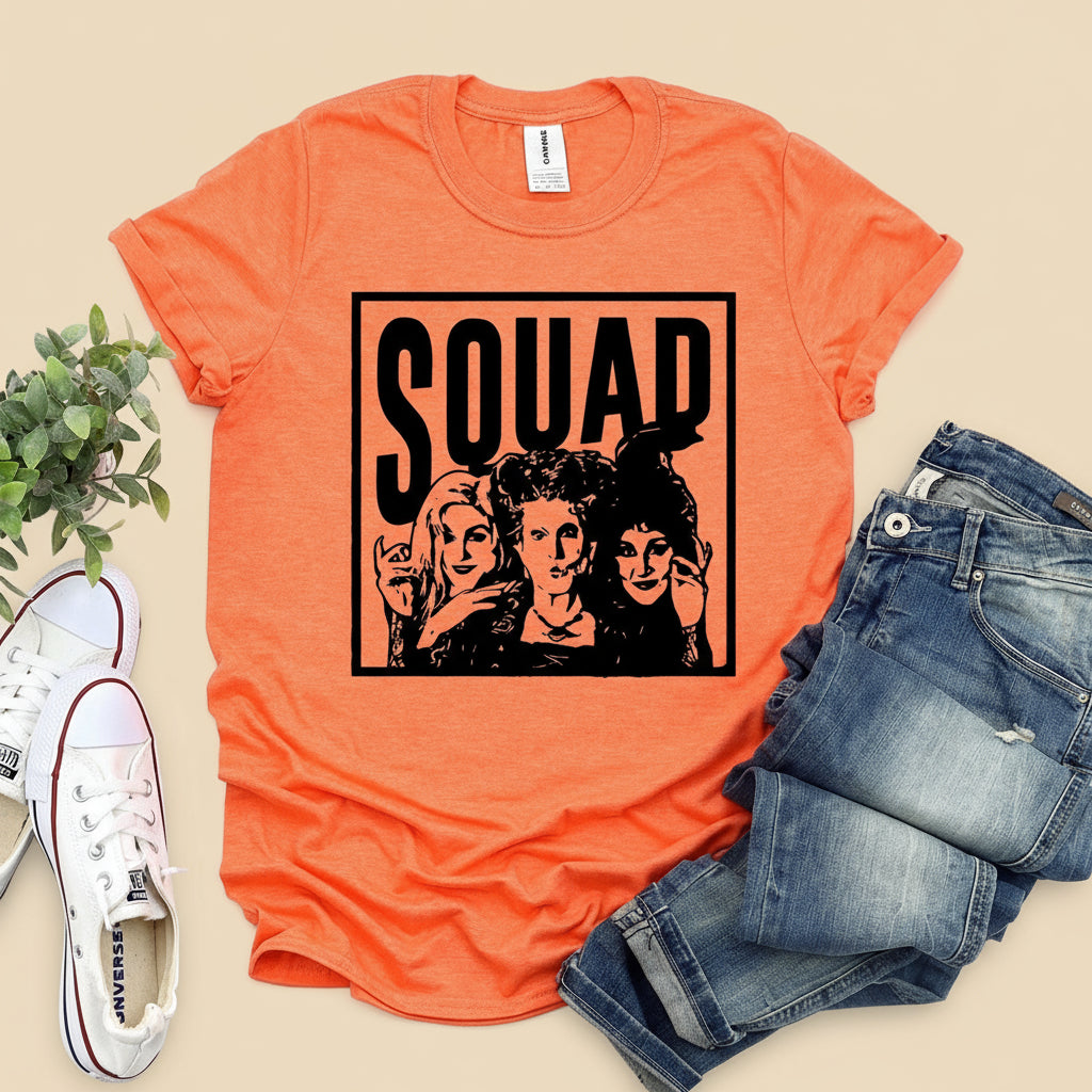 Orange t-shirt with 'SQUAD' graphic featuring three women, paired with jeans and sneakers on a wooden surface.