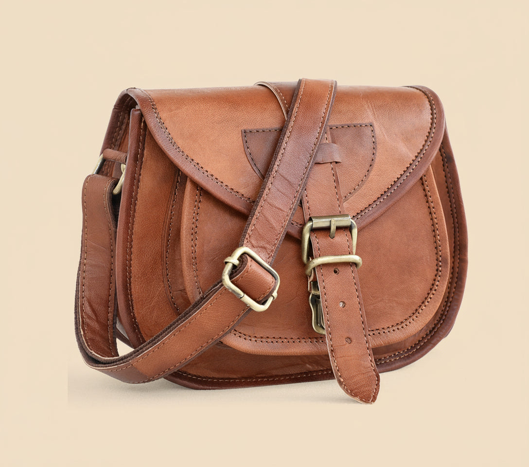 Brown leather satchel bag with gold buckle on a tan background