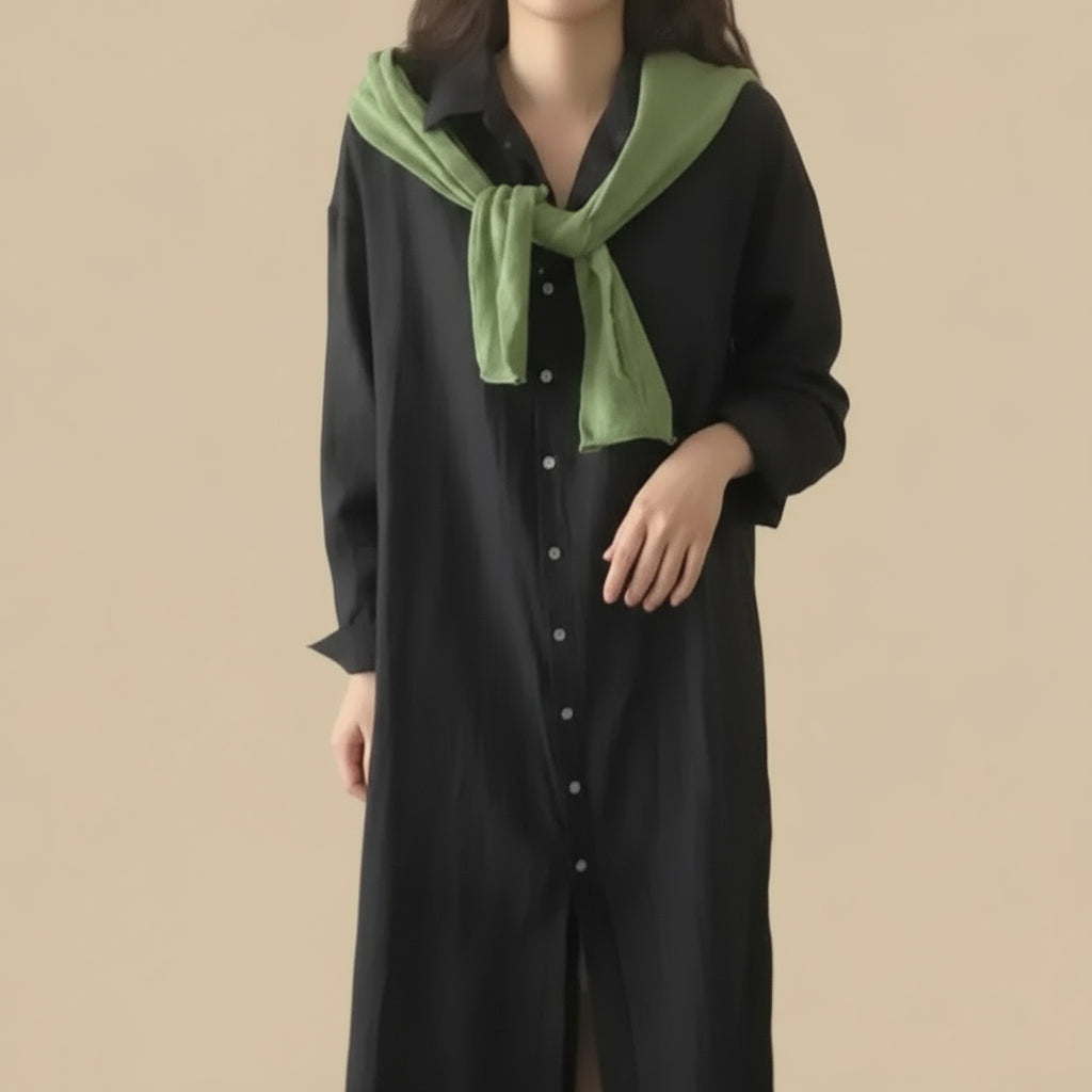 Person wearing a black dress with a green scarf in a room.