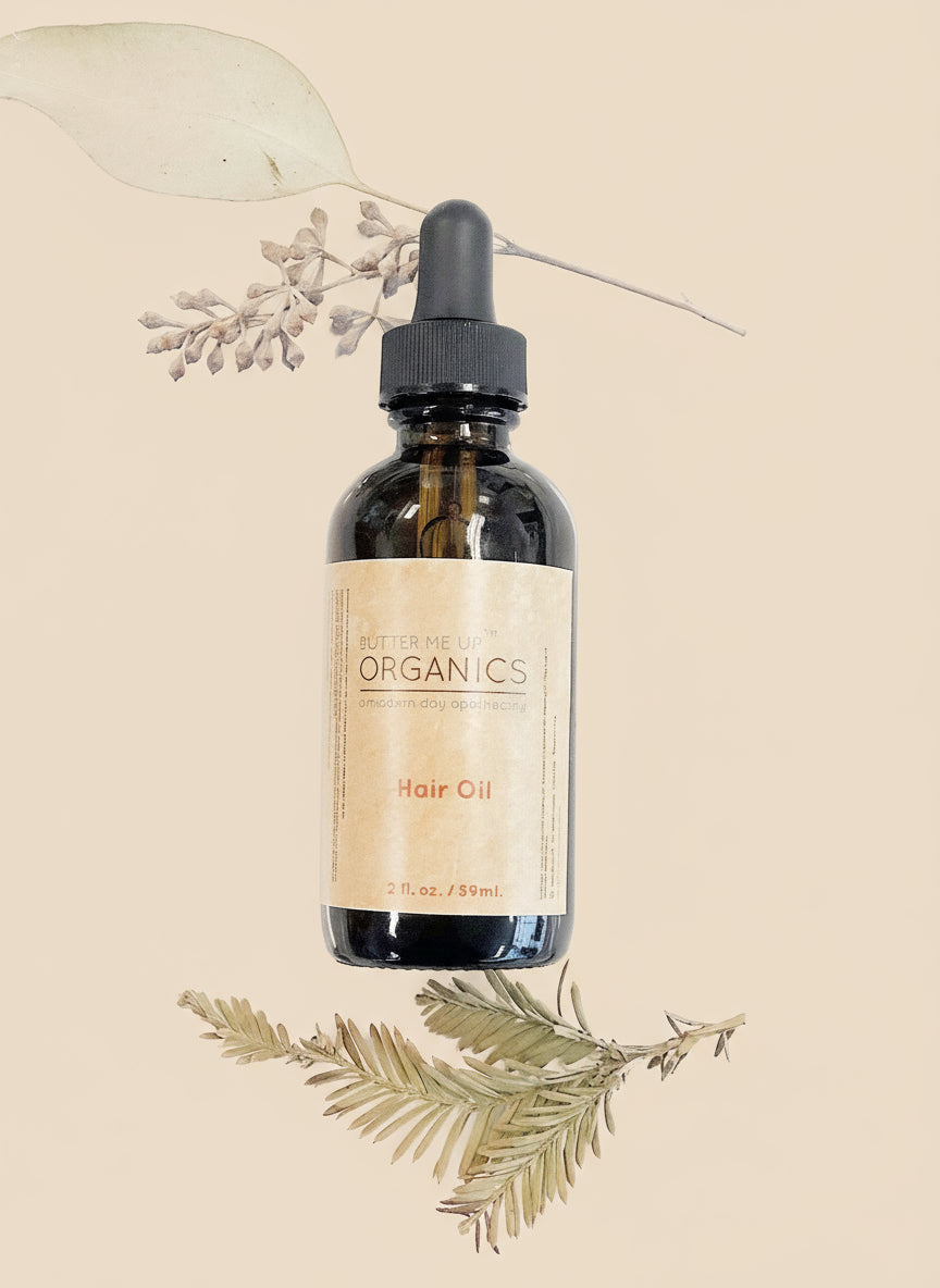 Bottle of hair oil with a dropper labeled 'Organics' on a white background with dried leaves.