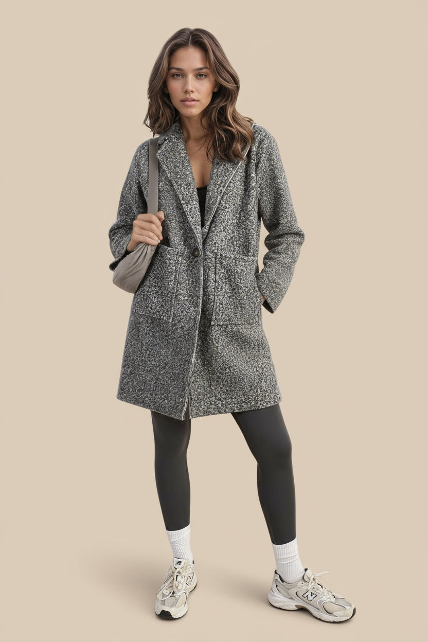 Woman in a gray coat standing outdoors with a tan
 background