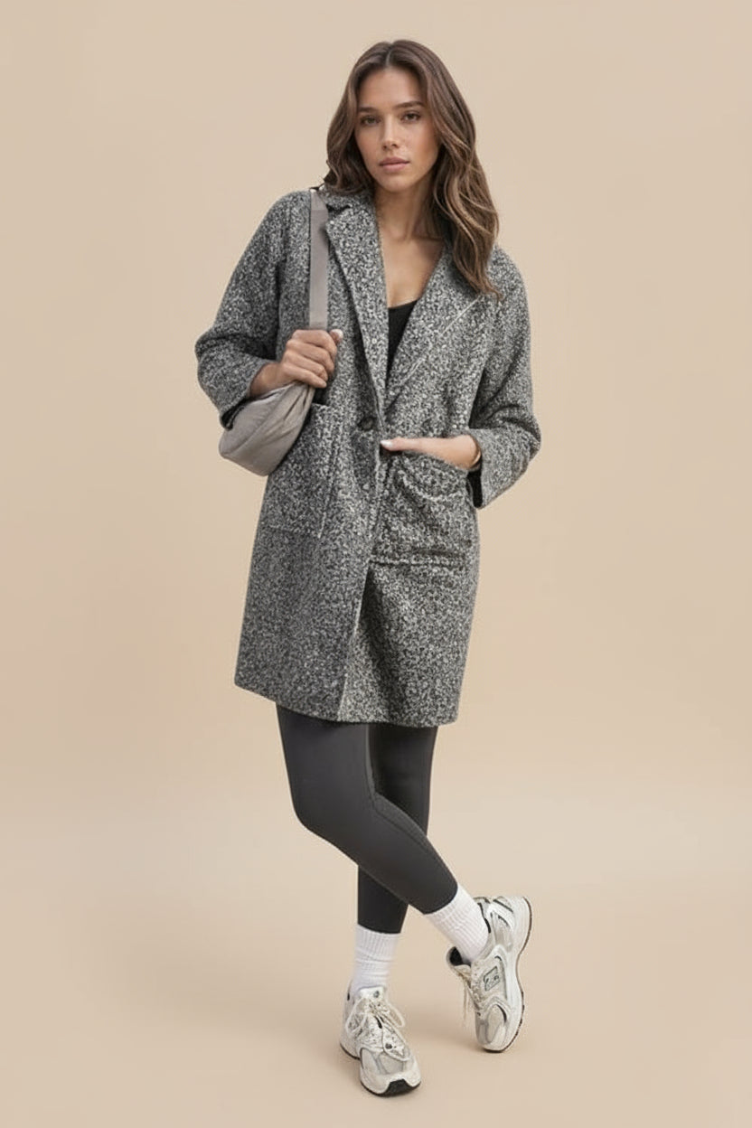 Woman in a gray coat standing with a tan background.