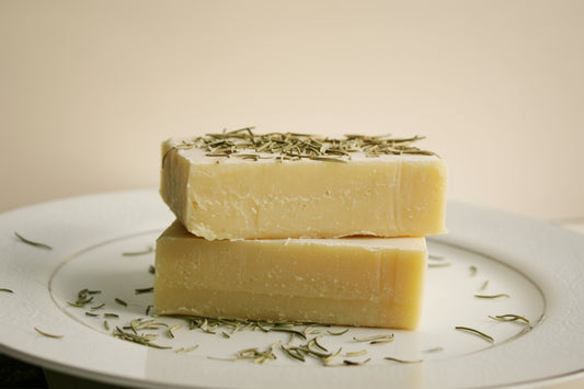 Two bars of soap with green herbs on a white plate against a beige background