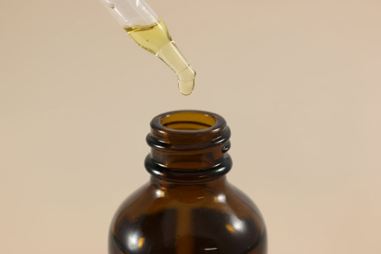 Brown glass bottle of hair oil with a dropper on a tan background