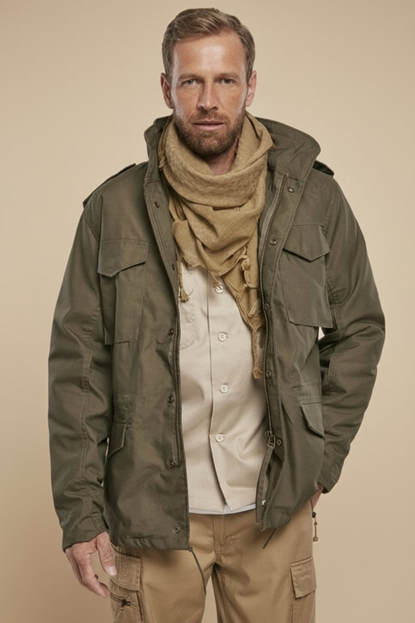 Man wearing a green jacket, beige scarf, and pants on a tan background