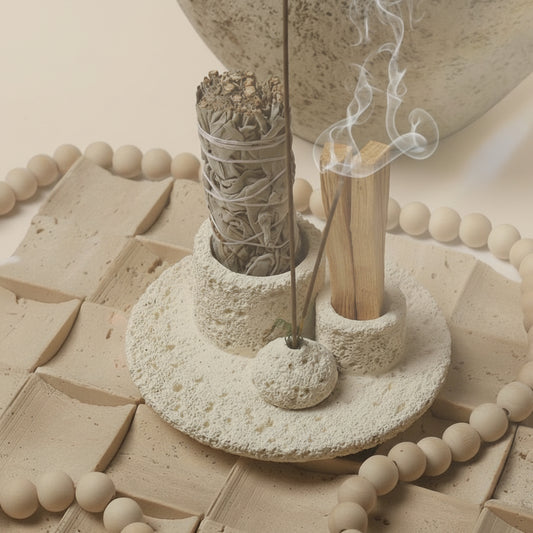 Ceramic incense holder with sage and wooden sticks on a textured surface.
